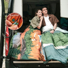 Zwei junge Personen sitzen zusammen in einem Lieferwagen, eingehüllt in bunte Decken, mit einem Basketball an der Seite