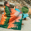 Zwei Personen sitzen auf dem Boden, eingewickelt in eine orange-grüne Decke mit Baum-Motiv, im Freien vor einer Felswand