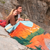 Ein Paar sitzt auf einem Felsen und hält eine bunte Decke mit Bergmotiv