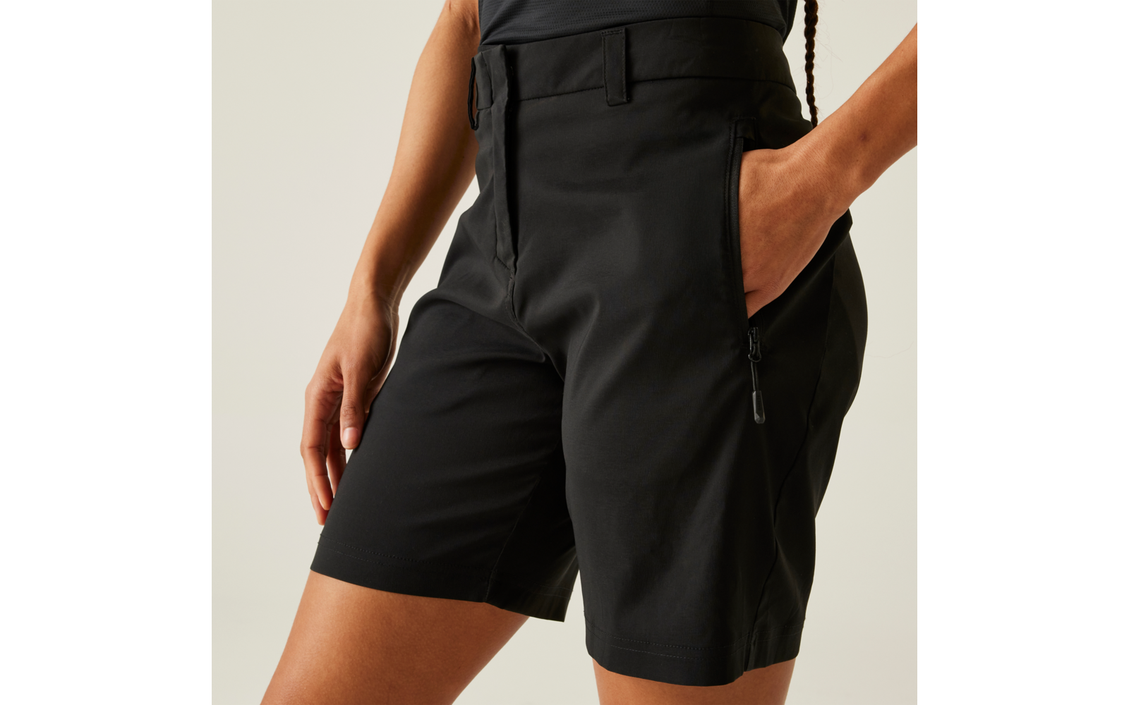 Schwarze, bis zur Mitte des Oberschenkels reichende Shorts mit Reißverschlusstasche; rechte Hand in der Tasche, linke Hand an der Seite; Bild auf Taille beschnitten