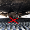 Een kat zit onder een voertuig op een roosteroppervlak, met een rood kruis over de kat