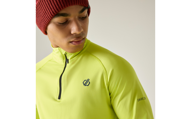 Personne portant un haut de sport manches longues jaune-vert vif avec demi-fermeture éclair, logo sur la poitrine et texte sur la manche, bonnet rouge en tricot, regard vers le bas à gauche