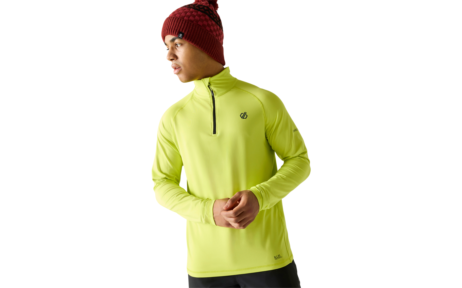 Personne portant un bonnet en tricot rouge à motif avec pompon et un haut manches longues jaune néon à fermeture éclair courte, petits logos sur poitrine et ourlet, mains jointes, regarde vers la gauche, pantalon foncé, fond blanc