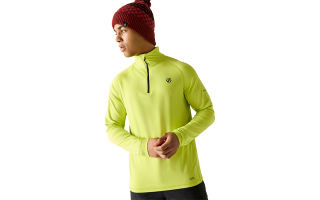 Personne portant un bonnet en tricot rouge à motif avec pompon et un haut manches longues jaune néon à fermeture éclair courte, petits logos sur poitrine et ourlet, mains jointes, regarde vers la gauche, pantalon foncé, fond blanc