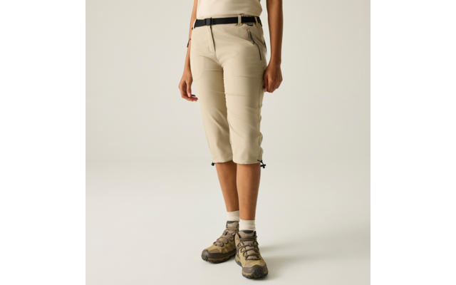 Unterkörper einer Person in knielanger beiger Hose, schwarzem Gürtel, weißen Socken und braunen Schuhen, Hände seitlich, heller Hintergrund