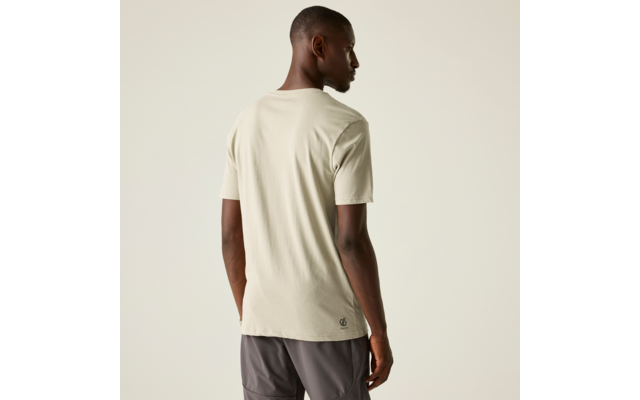 Person von hinten, trägt hellbeiges T‑Shirt und dunkle Shorts, steht vor hellem einfarbigem Hintergrund, Kopf leicht nach rechts gewandt