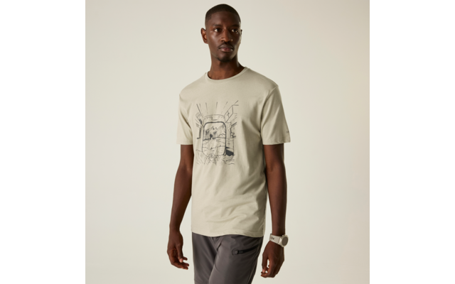 Mann steht vor neutralem Hintergrund, trägt hellbeiges T‑Shirt mit schwarzer Linienzeichnung vorn, dunkelgraue Hose und weiße Armbanduhr am linken Handgelenk