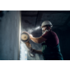 Mann mit Schutzhelm und Maske schleift an einer Wand mit einer Handschleifmaschine