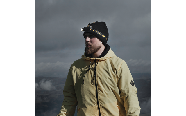 Mann mit gelber Jacke und Stirnlampe vor bewölktem Himmel