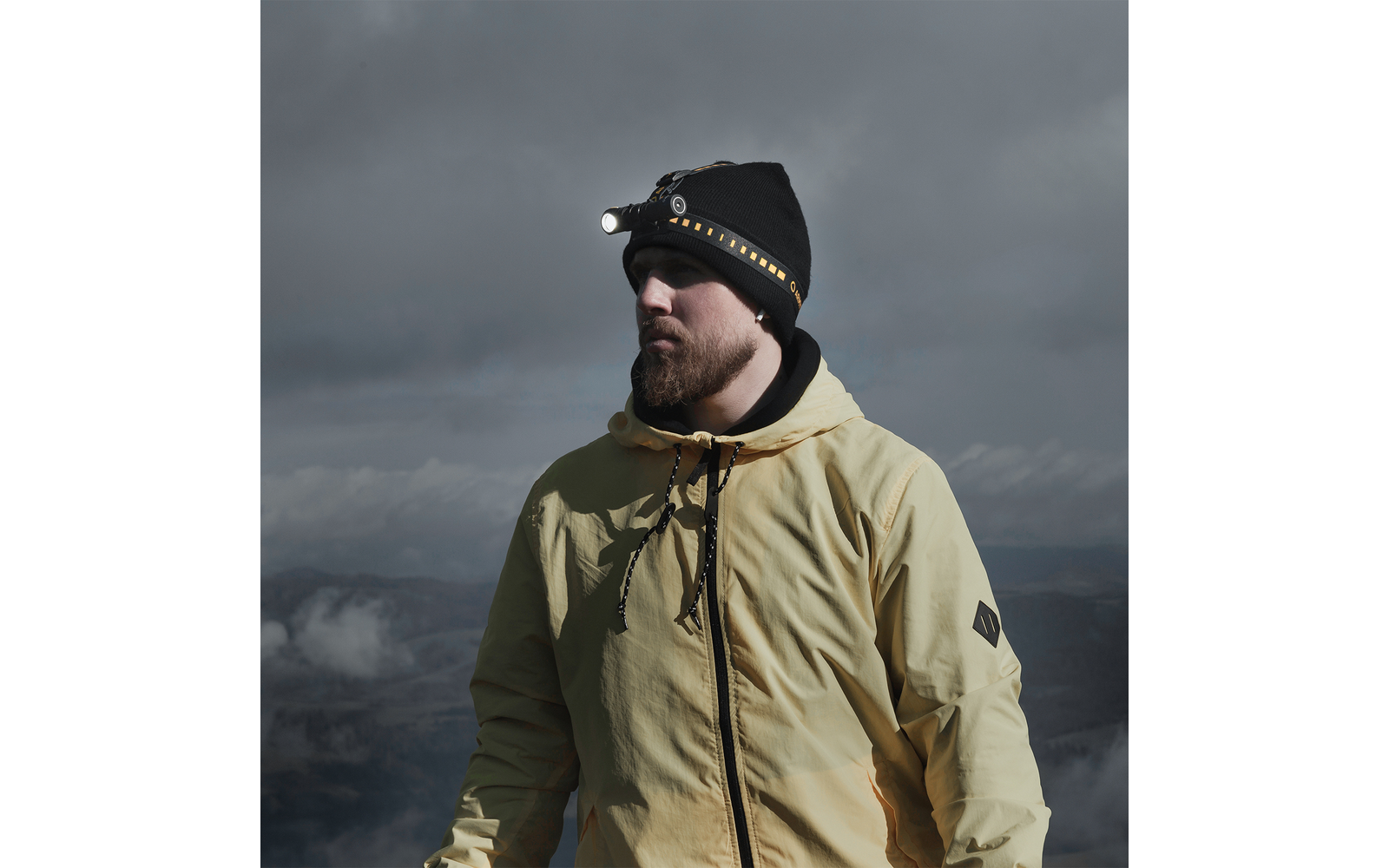 Mann mit gelber Jacke und Stirnlampe vor bewölktem Himmel