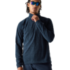 Persoon met gevlochten haar en spiegelende zonnebril, draagt donkerblauw fleece met hoge kraag en halve rits; één hand pakt de rits, witte achtergrond