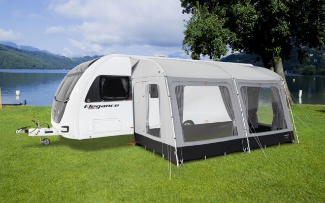 Roulotte con tenda annessa su un prato accanto a un lago