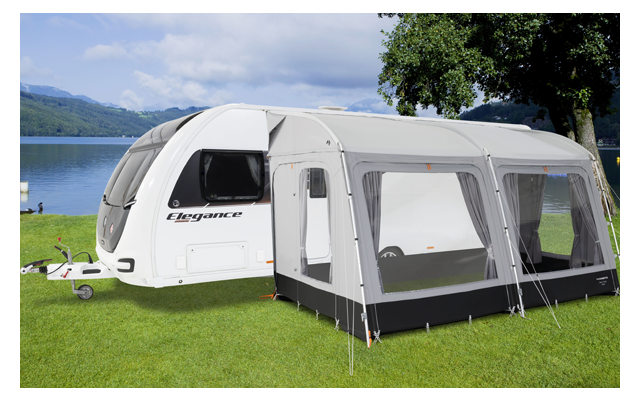 Caravana con toldo adjunto en un área de césped junto a un lago