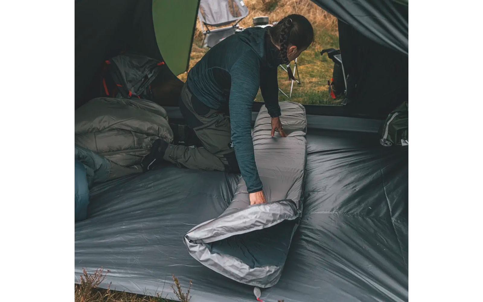 Person faltet eine graue Matratze in einem Zelt zusammen