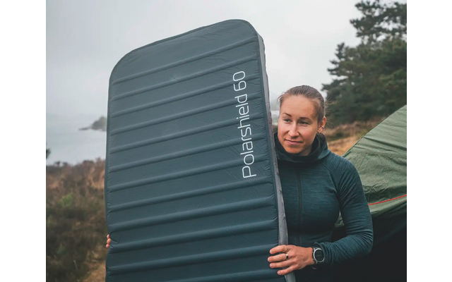 Person mit dunklem Pullover hält großen, dunkelblauen Koffer vor einem bewölkten Himmel