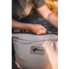 Mains tirant une fermeture éclair d'un sac matelassé beige clair avec un écusson 'BENT' ; personne portant un T-shirt gris foncé à manches courtes ; arrière-plan flou d'herbe