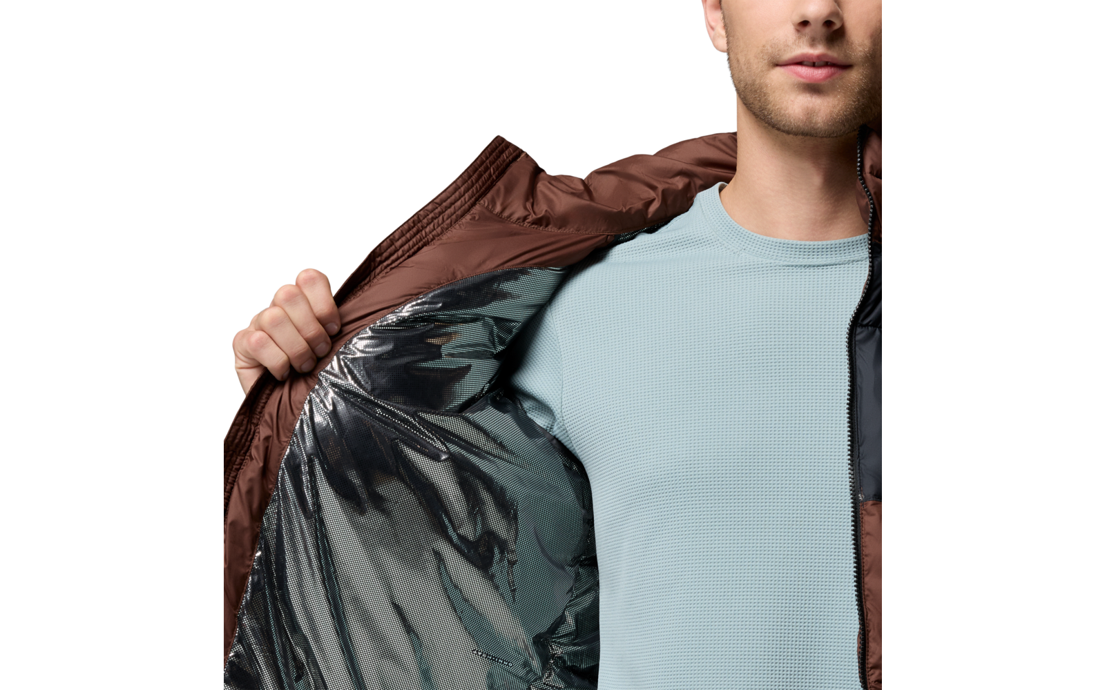 Person von Brust bis Kinn öffnet eine braune Jacke; silbernes Innenfutter und hellblaues Shirt sichtbar