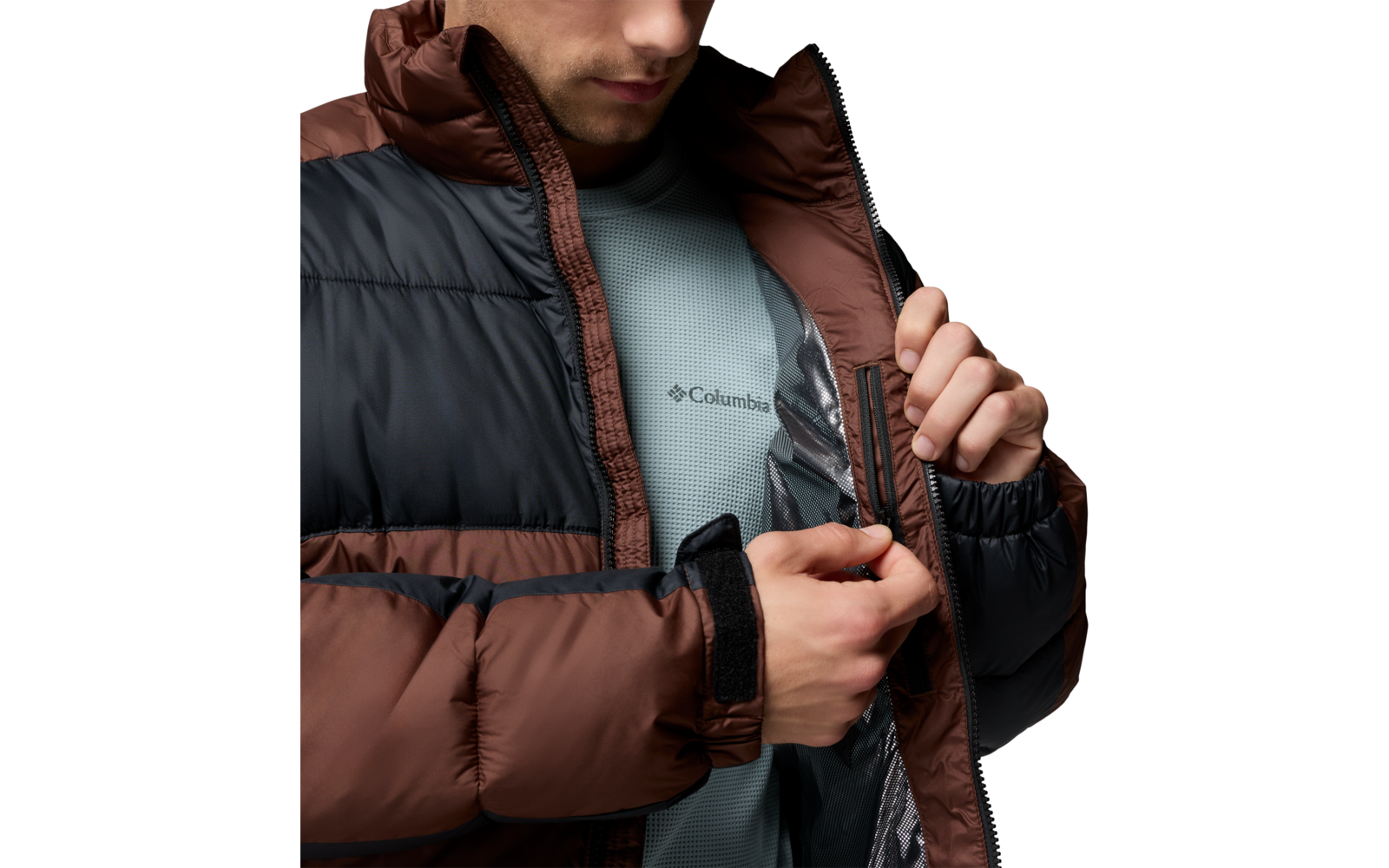 Teilansicht einer Person, die eine braun-schwarze Steppjacke öffnet; darunter ein hellblaues T-Shirt mit Columbia-Logo sichtbar