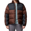 Person trägt braun-schwarze Steppdaunenjacke, hellblaues T‑Shirt und graue Hose, vor weißem Hintergrund