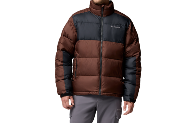 Person trägt braun-schwarze Steppjacke mit Columbia-Logo, steht mit Händen an den Seiten, schaut nach rechts, trägt graue Hose
