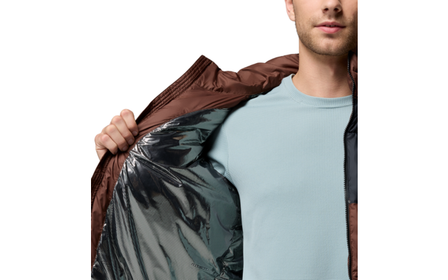 Person von Brust bis Kinn öffnet eine braune Jacke; silbernes Innenfutter und hellblaues Shirt sichtbar