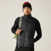 Person in schwarzer Steppweste und schwarzem Langarmshirt, schwarze Mütze mit aufgesetzter Sonnenbrille, hält grünen Rucksackriemen, heller Hintergrund