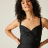 Personne aux cheveux bouclés et foncés portant un maillot une-pièce noir sans manches, mains sur les hanches, léger sourire
