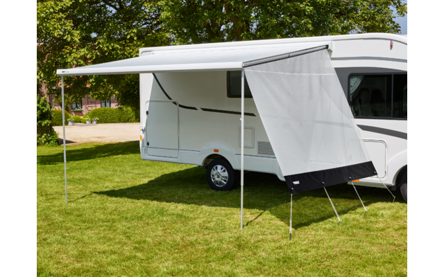 Weißes Wohnmobil mit ausgefahrener Markise und befestigtem Sichtschutz, zwei Stützstangen, Grasfläche und Bäume im Hintergrund