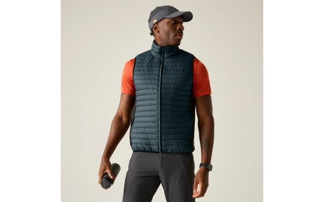 Person mit grauer Kappe, orangefarbenem Kurzarmshirt und dunkler gesteppter Weste, hält eine Trinkflasche, trägt eine Uhr am linken Handgelenk, Blick zur Seite, heller einfarbiger Hintergrund