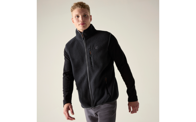 Mann trägt schwarze Fleeceweste mit Reißverschluss, schwarzes Langarmshirt und graue Hose vor hellem Hintergrund