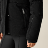 Schwarze gesteppte Cordjacke mit Reißverschlusstasche, schwarze Hose, sichtbare Hand mit kleinem Fingertattoo