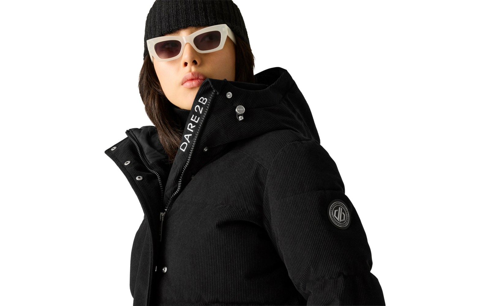 Person mit weißer Sonnenbrille, schwarzer Strickmütze und schwarzer gesteppter Jacke mit Kapuze, Reißverschluss mit Schriftzug 'DARE2B' und rundem Logo-Patch auf dem Ärmel; Gesicht teilweise sichtbar