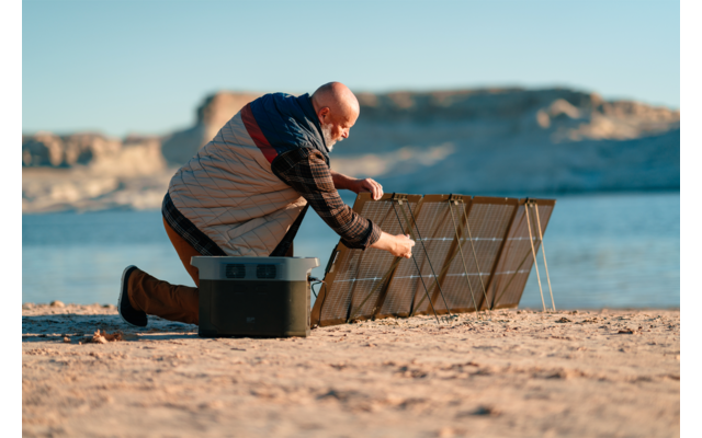 Person sitzt auf dem Boden am Strand und hält ein Tablett