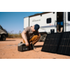 Mann kniet auf Boden vor Solarpanel und öffnet Werkzeugkoffer, im Hintergrund Wohnmobil