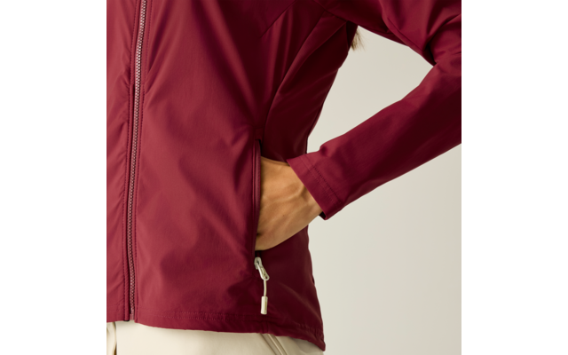 Gedeeltelijke weergave van een persoon met een donkerrode jas, hand in zijzak, zichtbare ritssluiting, lichtgekleurde broek, lichte effen achtergrond