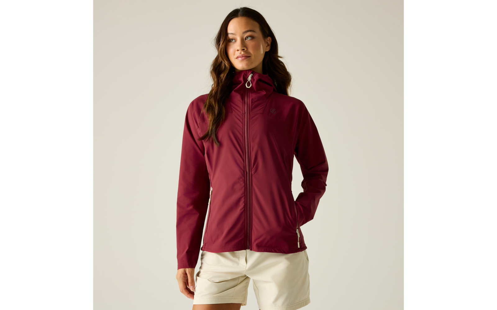 Vrouw met bordeaux capuchonjas (gesloten) en witte korte broek, staand voor een lichte achtergrond, kijkt opzij