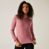 Frau mit lockigem Haar trägt einen rosa Pullover und steht vor weißer Wand
