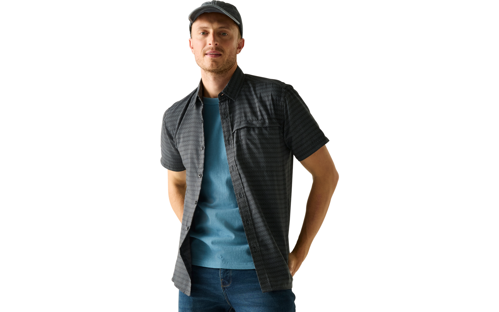 Stehender Mann mit dunkelgrauer Baseballkappe, offenes dunkles kurzärmeliges Hemd über blauem Pullover, Jeans, Hände in den Hosentaschen, heller Hintergrund