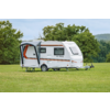 Witte caravan met uitgeklapte luifel en open deur op een grasveld, bomen op de achtergrond
