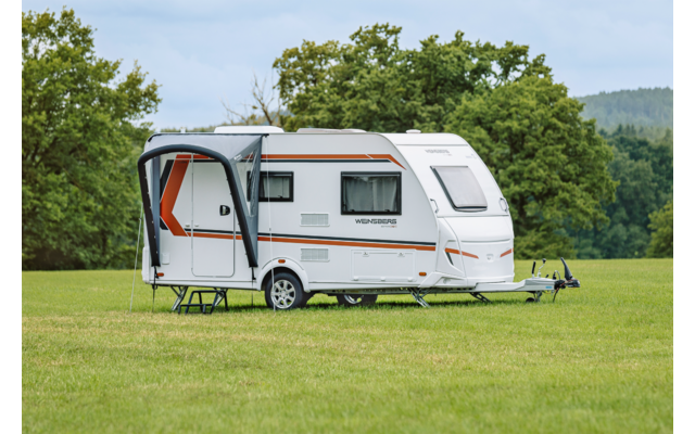 Witte caravan met uitgeklapte luifel en open deur op een grasveld, bomen op de achtergrond
