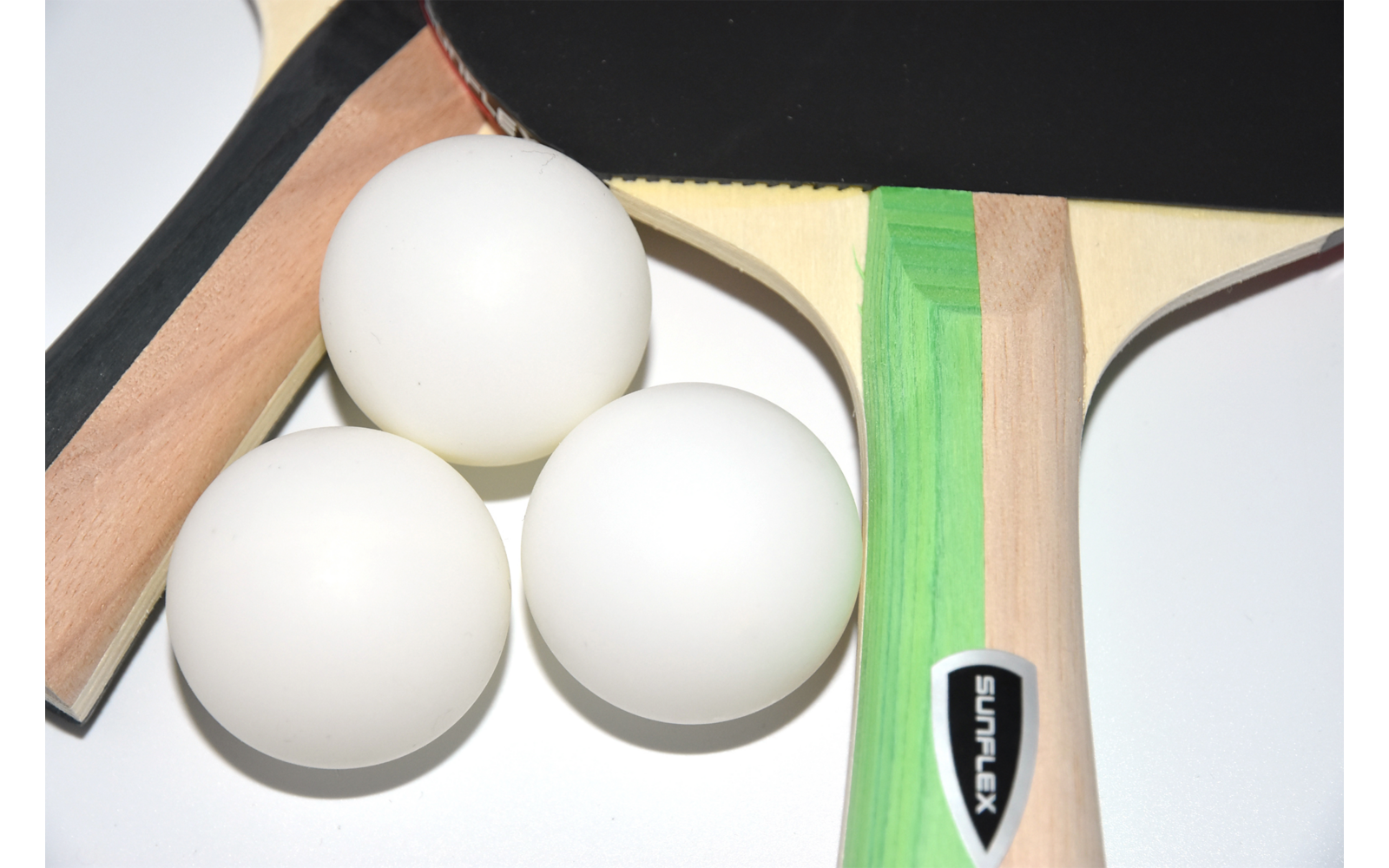 Vier weiße Tischtennisbälle liegen neben zwei Tischtennisschlägern auf einem dunklen Untergrund