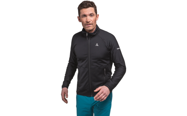 Stehende Person in schwarzer Jacke mit Reißverschluss und kleinem weißem Logo auf der Brust, türkisfarbene Hosen, weißer Hintergrund