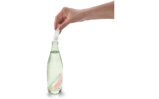 Hand hält einen Glasflaschenverschluss über einer geöffneten Glasflasche mit klarer Flüssigkeit