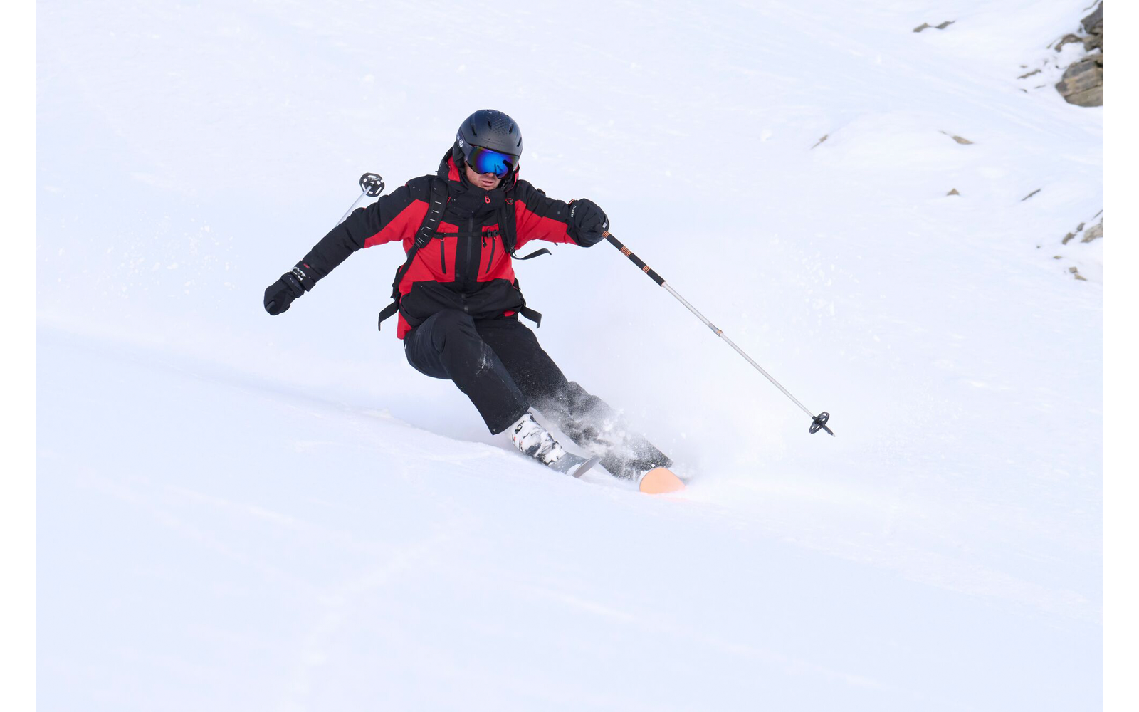 Person fährt Ski im Schnee mit roter Jacke und blauem Helm