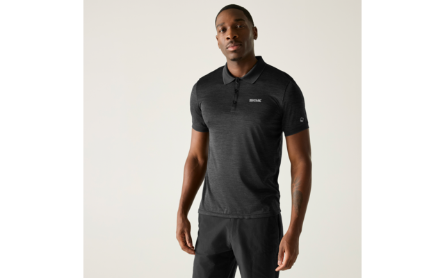 Man met donkergrijs poloshirt met korte mouwen en klein logo op de borst en donkere broek, staand voor een lichte effen achtergrond; zichtbare tatoeage op de onderarm