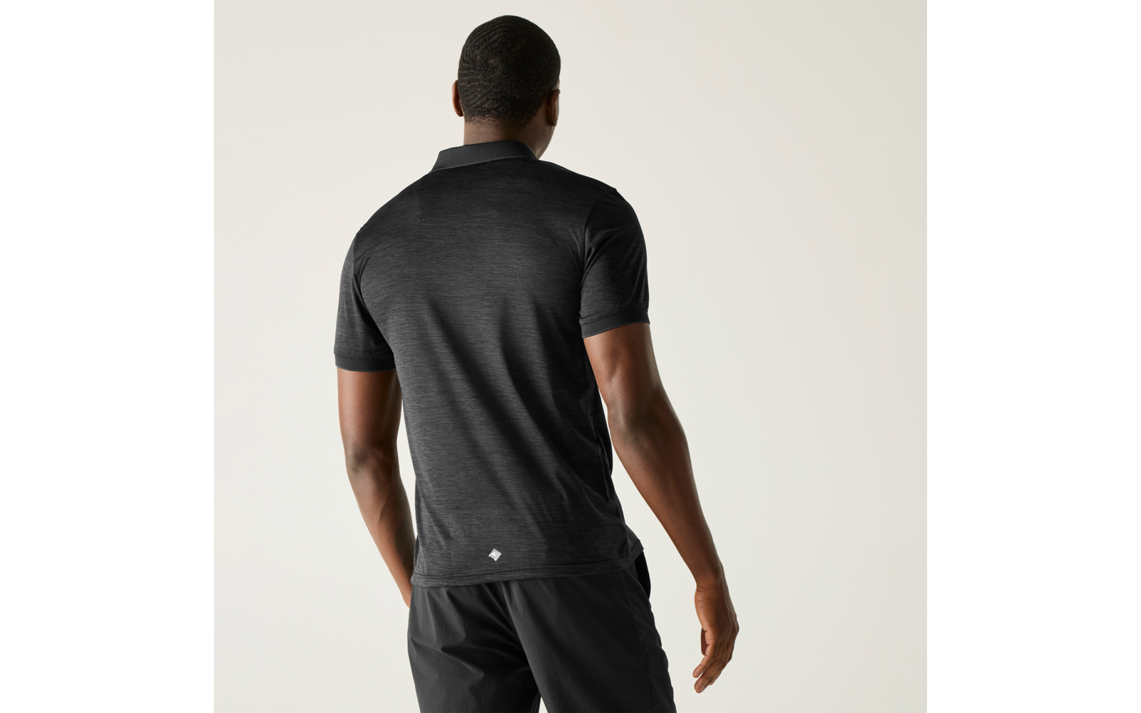 Persoon van achteren, zwart poloshirt en zwarte shorts, lichte effen achtergrond