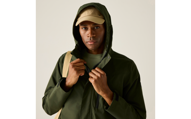 Person mit hochgezogener dunkelgrüner Kapuzenjacke, beiger Baseballkappe, grünem T‑Shirt und beigem Rucksackriemen, hält den Reißverschluss