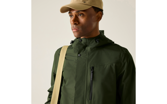 Person mit beigefarbenem Baseballcap, dunkelgrüner Regenjacke mit Reißverschluss und hellbeigem Schultergurt vor hellem Hintergrund