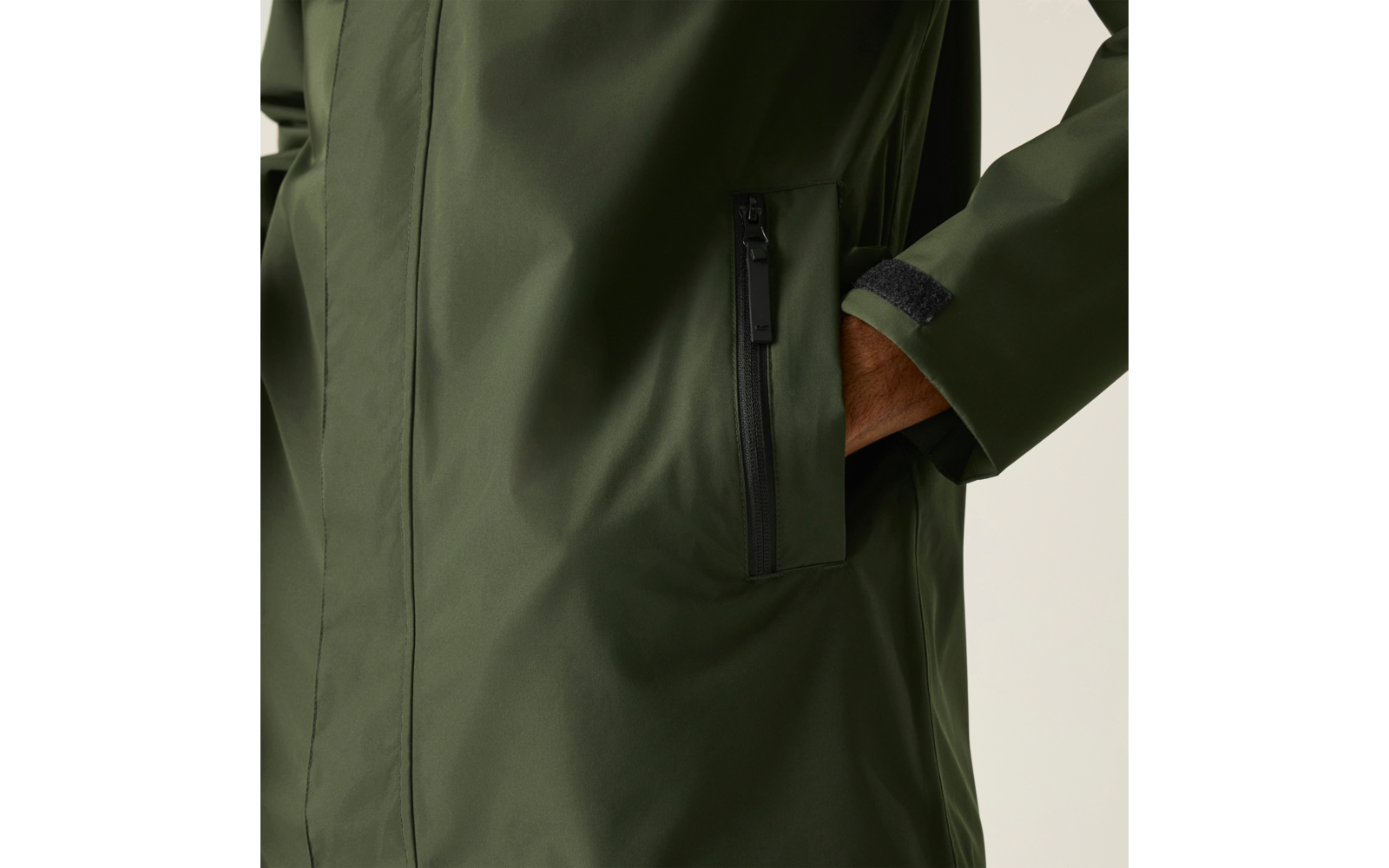 Hand in Reißverschlusstasche eines olivgrünen Mantels, Ärmel mit Klettverschluss sichtbar