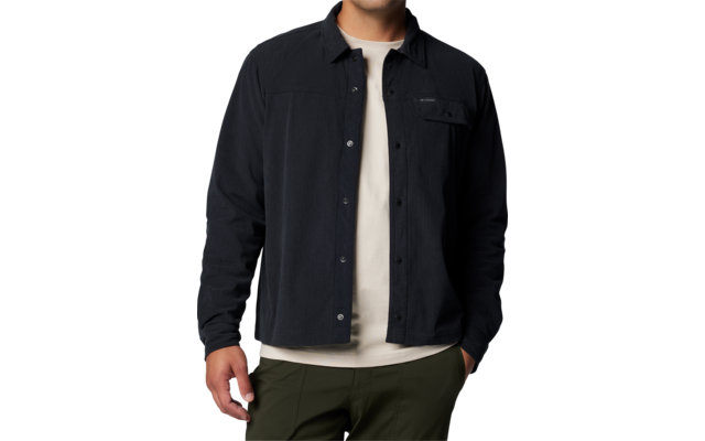 Homme debout regardant l'appareil photo, portant une surchemise noire sur un T-shirt blanc et un pantalon vert olive sur fond blanc